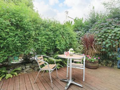 A small patio with two metal chairs and a round table with cups and flowers surrounded by plants at Bolitho's Retreat in Helford