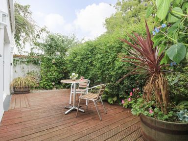 A wooden deck with a round table and two chairs surrounded by greenery at Bolitho's Retreat in Helford