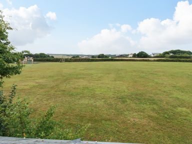 A large grassy field with some trees and playground equipment in the distance at Bolitho's Retreat in Helford