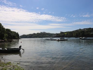 A calm river with boats floating and a tree-covered shoreline at Bolitho's Retreat in Helford
