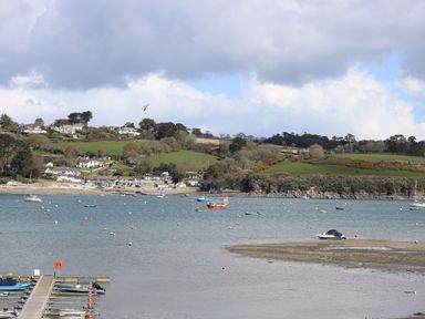 A coastal scene showing boats on the water with houses and green hills in the background at Bolitho's Retreat in Helford