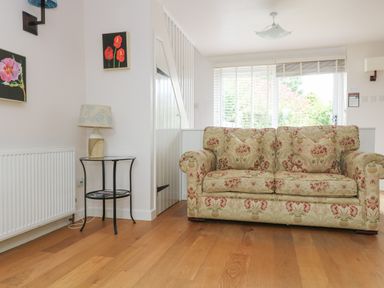 A living room with a patterned sofa a small round table with a lamp and two flower paintings on the wall at Bolitho's Retreat Helford