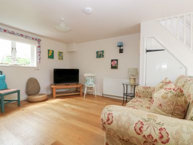 A living room with a floral sofa a television on a wooden stand various chairs and paintings on the wall at Bolitho's Retreat in Helford