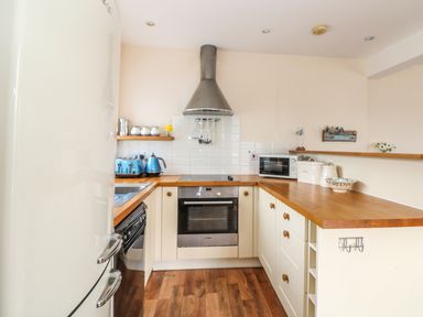 A kitchen with wooden countertops white cabinets a toaster kettle oven microwave and a refrigerator at Bolenowe Trebetherick near Polzeath