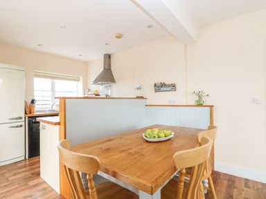 A kitchen area with a wooden dining table and chairs and a bowl of green apples at Bolenowe in Trebetherick near Polzeath