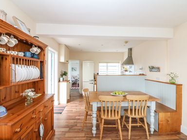 A kitchen with a wooden dining table and chairs next to a wooden cabinet with dishes at Bolenowe in Trebetherick near Polzeath