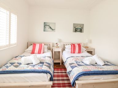 A bedroom with two single beds with patterned quilts and red striped pillows at Bolenowe in Trebetherick near Polzeath