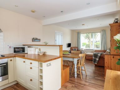A kitchen with a microwave and dining table next to a living room with a sofa and window at Bolenowe Trebetherick near Polzeath