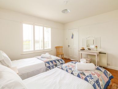 A bedroom with two single beds a wooden chair a dressing table with a mirror and a window with blinds at Bolenowe Trebetherick near Polzeath
