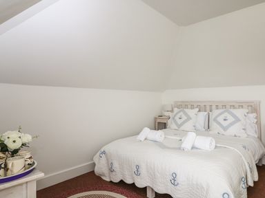 A bedroom with a bed covered in a white quilt and pillows with anchor patterns and rolled white towels on the bed at Bolenowe Trebetherick near Polzeath
