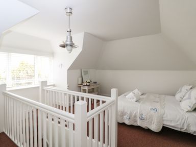 A bedroom with a bed with anchor patterned bedspread and pillows, a white railing around stairs and a small table with a mirror at Bolenowe in Trebetherick near Polzeath