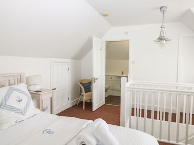 A bedroom with a bed side table and lamp a wicker chair an open door to a bathroom and white wooden railings at Bolenowe Trebetherick near Polzeath