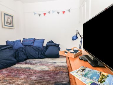 A room with blue cushions and bean bags on a rug and a wooden TV stand with a lamp and magazines at Bolenowe Trebetherick near Polzeath