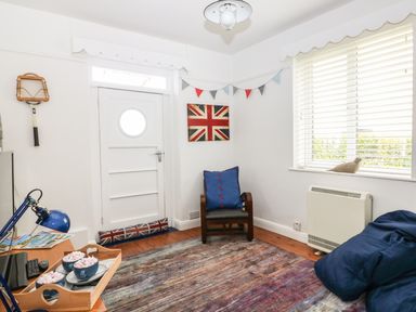 A small sitting room with a wooden chair with a blue cushion a blue bean bag and a tray with cups on a table near a white door and window at Bolenowe in Trebetherick near Polzeath