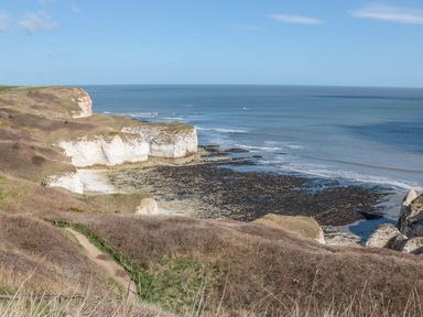 A coastal cliff with a dirt path leading to rocky shores and the sea at Lilly May Cottage in Flamborough