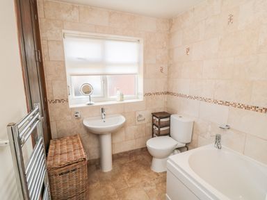 A bathroom with a sink toilet bathtub wicker laundry basket and window at Lilly May Cottage in Flamborough