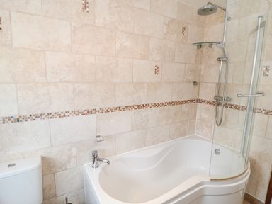 A bathroom with a white bathtub shower combination and tiled walls at Lilly May Cottage in Flamborough