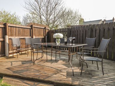 An outdoor wooden deck with a glass table and six metal chairs surrounded by wooden fences at Lilly May Cottage in Flamborough