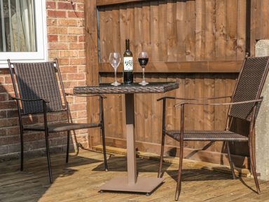 A small outdoor seating area with two wicker chairs a square table a bottle of wine and two wine glasses at Lilly May Cottage in Flamborough