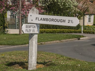 A road sign on a grassy patch showing directions to Flamborough Bempton and Filey with houses and trees in the background at Lilly May Cottage in Flamborough