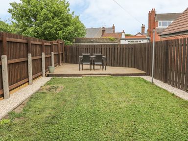 A backyard with grass a wooden deck with a table and four chairs and wooden fences at Lilly May Cottage in Flamborough
