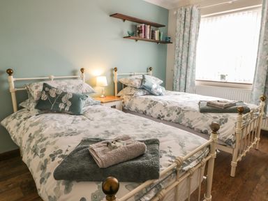A bedroom with two single beds side by side with patterned bedding and pillows a nightstand with a lamp between the beds and shelves with books on the wall at Lilly May Cottage in Flamborough