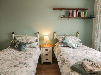 A bedroom with two single beds a small bedside table with a lamp and wall shelves with books at Lilly May Cottage in Flamborough