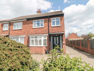 A brick semi detached house with white windows a black front door and bushes in front at Lilly May Cottage in Flamborough