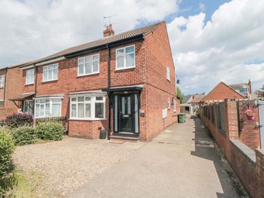 A brick semi detached house with a black front door and gravel driveway at Lilly May Cottage in Flamborough