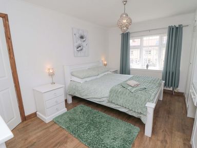 A bedroom with a double bed bedside tables lamps and green curtains at Lilly May Cottage in Flamborough