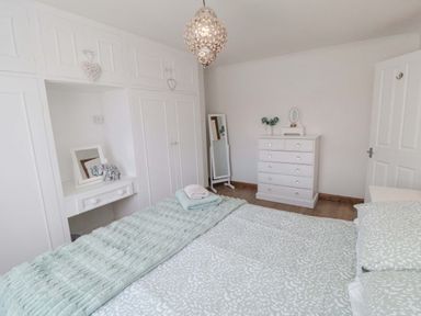 A bedroom with a bed covered in patterned bedding a chest of drawers a standing mirror and built in wardrobes at Lilly May Cottage in Flamborough