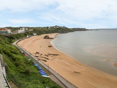 A sandy beach with boats on the grass by a walkway and houses on a hill at Apartment 2 in Tenby