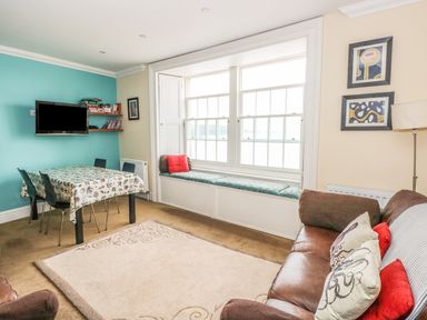 A living room with a dining table and chairs a television a window seat and a sofa with cushions at Apartment 2 in Tenby