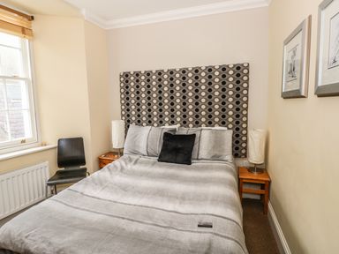 A bedroom with a double bed a patterned headboard two bedside tables with lamps a chair and framed pictures on the wall at Apartment 2 in Tenby