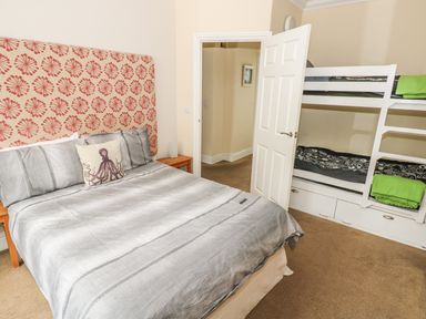 A bedroom with a double bed with gray bedding and an octopus pillow next to a white bunk bed with black and white bedding at Apartment 2 in Tenby