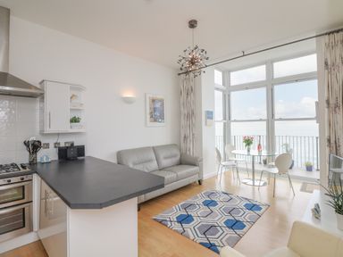 A living area with a kitchen counter sofa dining table and large windows overlooking the sea at Oceans Side in Ilfracombe