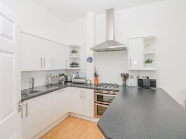A kitchen with white cabinets black countertops a gas stove and silver extractor at Oceans Side in Ilfracombe