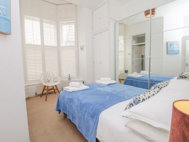 A bedroom with a bed covered in a blue blanket a white chair near shuttered windows and mirrored wardrobes at Oceans Side in Ilfracombe