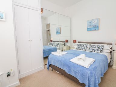 A bedroom with a bed covered in a blue blanket two nightstands with lamps a large mirror on the wall and a white wardrobe at Oceans Side in Ilfracombe