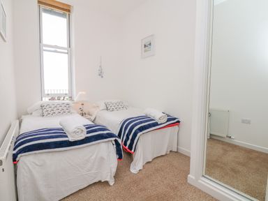 A small bedroom with two single beds a window and a mirror at Oceans Side in Ilfracombe