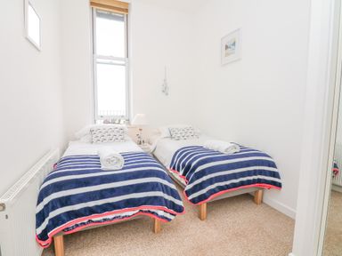 A bedroom with two single beds with striped blankets and a window between them at Oceans Side in Ilfracombe