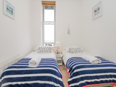 A bedroom with two single beds each with striped blankets and rolled towels beside a window at Oceans Side in Ilfracombe