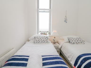 A bedroom with two single beds a window between them and a bedside table with a lamp at Oceans Side in Ilfracombe