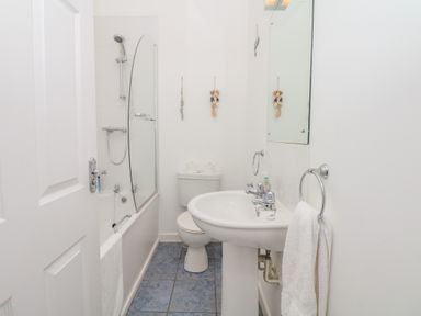 A bathroom with a bathtub with shower, toilet, sink, mirror, and towels at Oceans Side in Ilfracombe