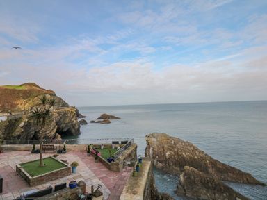 A coastal view with rocky cliffs a palm tree and seating area overlooking the sea at Oceans Side in Ilfracombe
