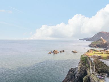 A coastal cliff with rocks in the sea and grassy land with stairs at Oceans Side in Ilfracombe