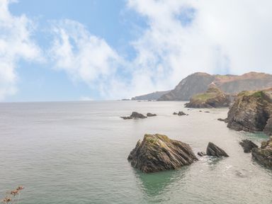 A coastal scene with rocky cliffs and calm sea under a partly cloudy sky at Oceans Side in Ilfracombe