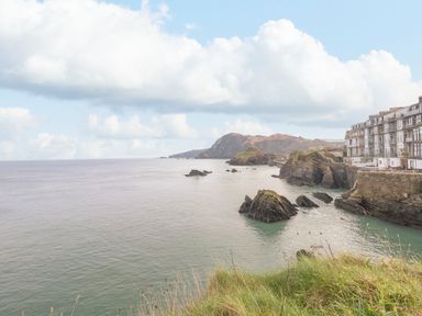 A coastal view with rocky cliffs and buildings near the shore at Oceans Side in Ilfracombe