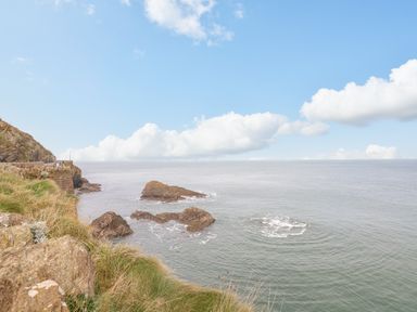 Rocky coastline with grassy cliffs and sea under a partly cloudy sky at Oceans Side in Ilfracombe