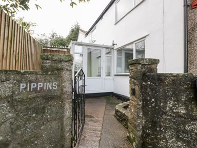 A pathway leading to a white house entrance with a glass porch behind stone walls and a black metal gate at Pippins in Bream